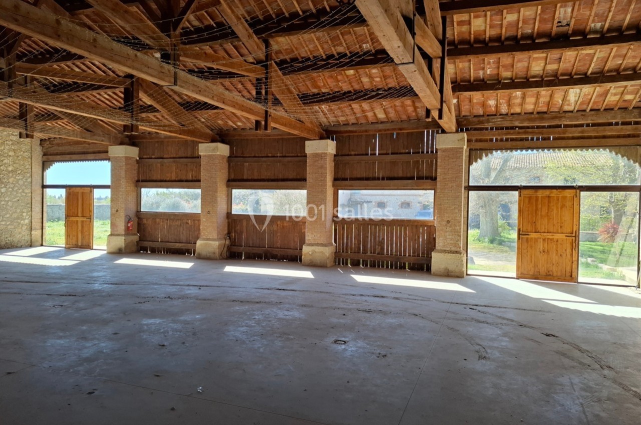 Intérieur d'une grange en bois avec de grandes ouvertures laissant entrer la lumière naturelle.