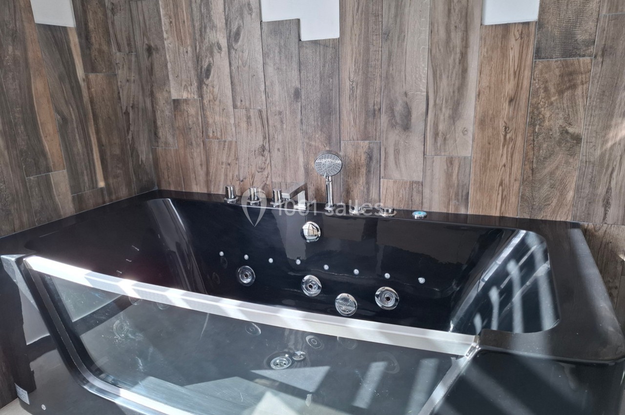 Baignoire noire moderne avec jets d'hydromassage, entourée de panneaux muraux en bois texturé.