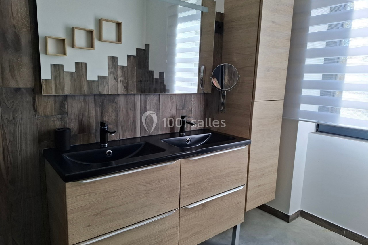 Double vasque moderne en bois clair avec miroir, robinetterie noire, et mur en bois décoratif dans une salle de bain…