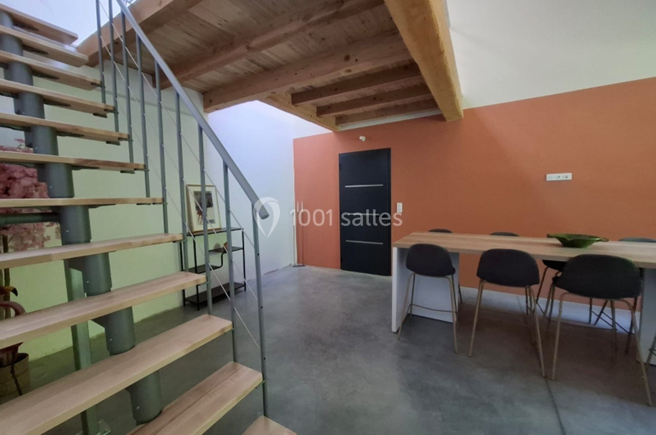 Escalier en bois et métal menant à une mezzanine, avec une table et des chaises dans une pièce aux murs orange.