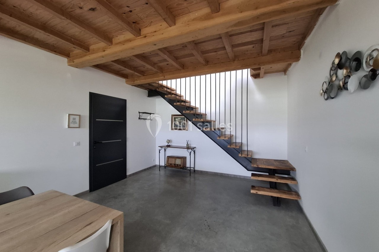 Escalier en bois et métal dans un intérieur moderne avec plafond en poutres apparentes et sol en béton ciré.