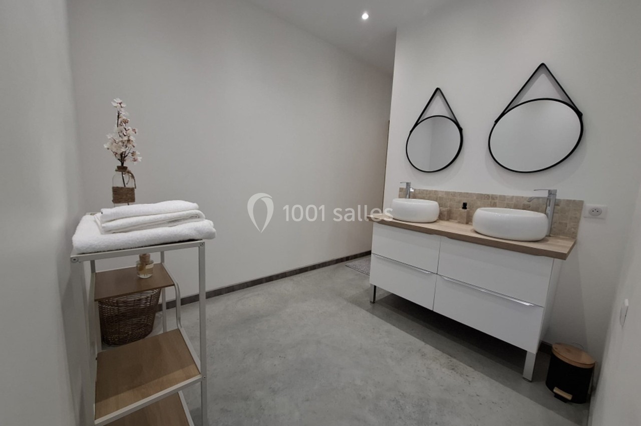 Salle de bain moderne avec deux vasques, miroirs ronds, étagère en bois et serviettes pliées.