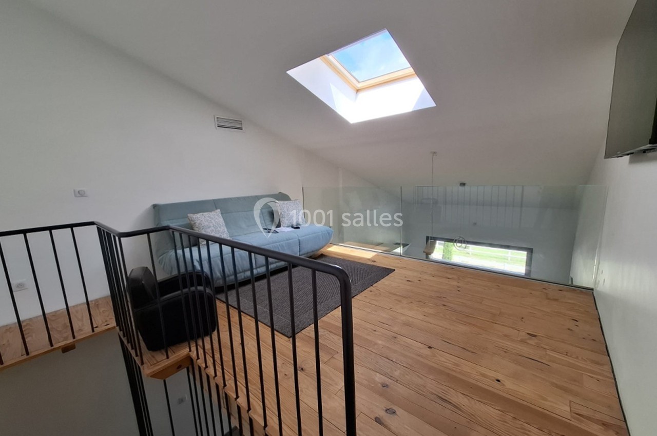 Mezzanine lumineuse avec parquet en bois, canapé bleu, tapis gris et grande fenêtre de toit.