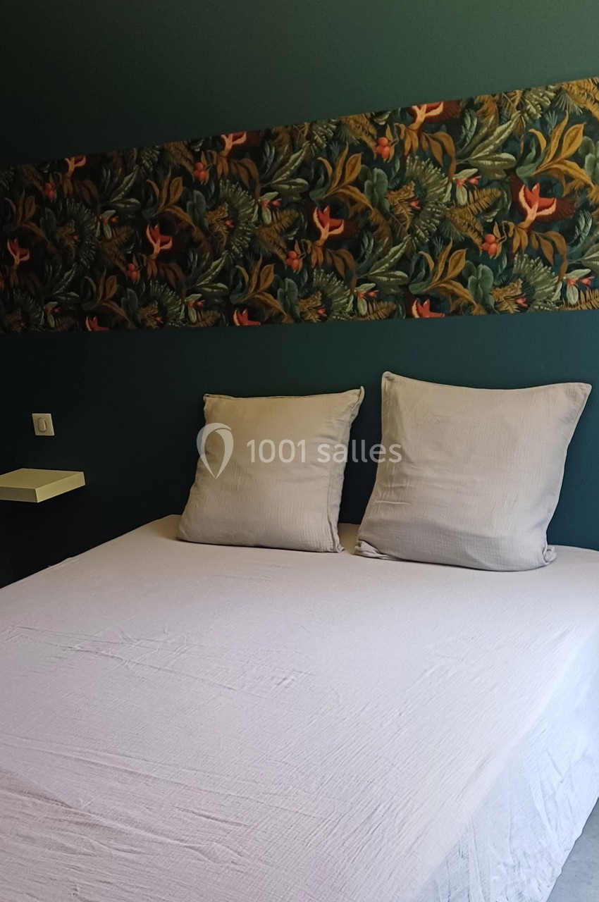 Lit double avec drap blanc, deux oreillers et une tête de lit ornée d'un motif floral sur fond vert.