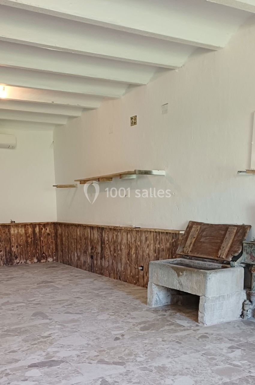 Une pièce vide avec murs blancs, étagères en bois, lambris bas et un ancien foyer en pierre au sol.