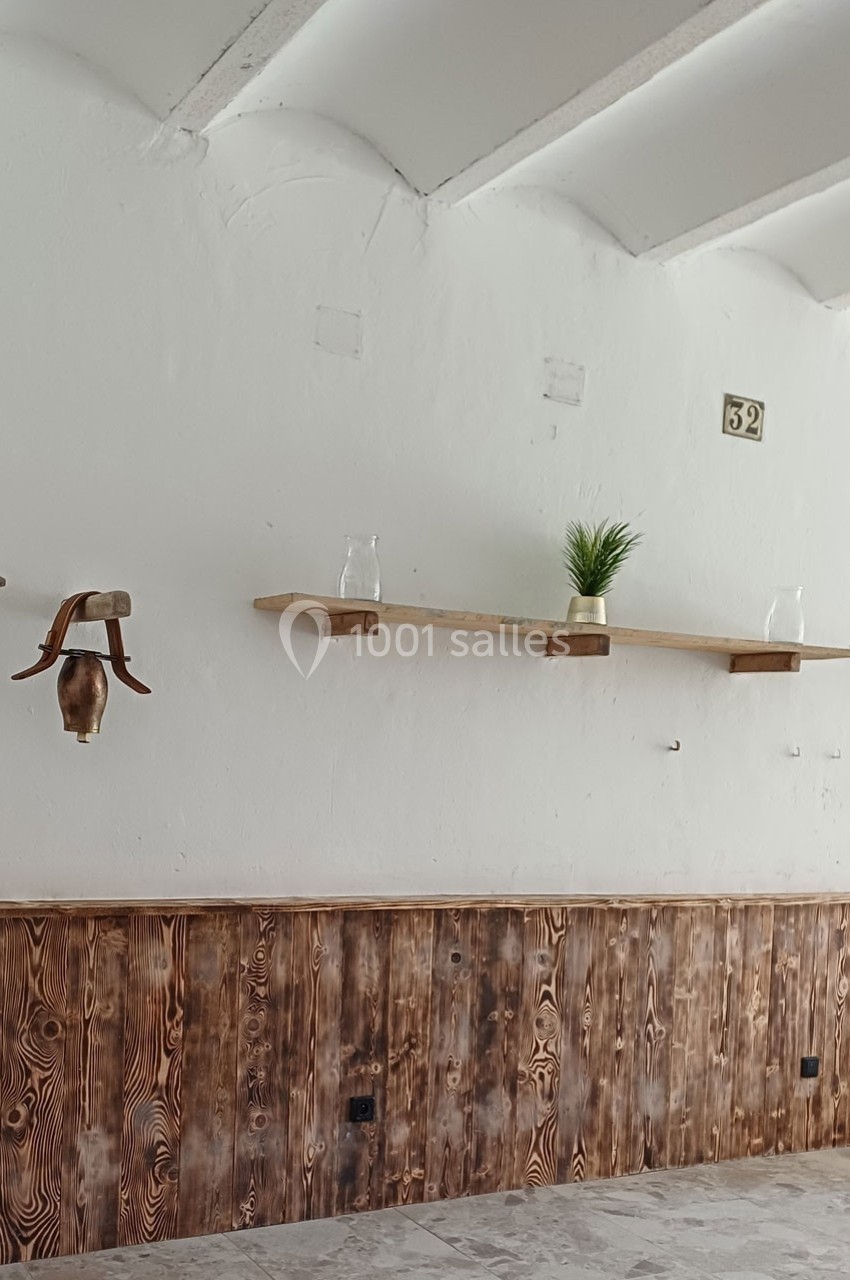 Mur intérieur avec étagères en bois, plante en pot, verres et applique murale, sur fond de lambris et plafond blanc.