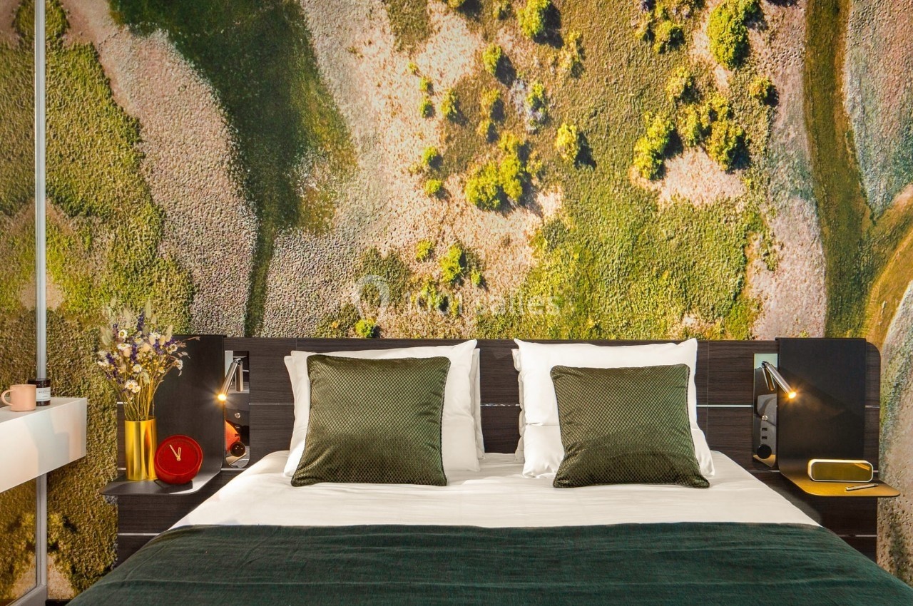 Lit double avec draps verts, coussins assortis et décoration murale représentant un paysage naturel vu du ciel.