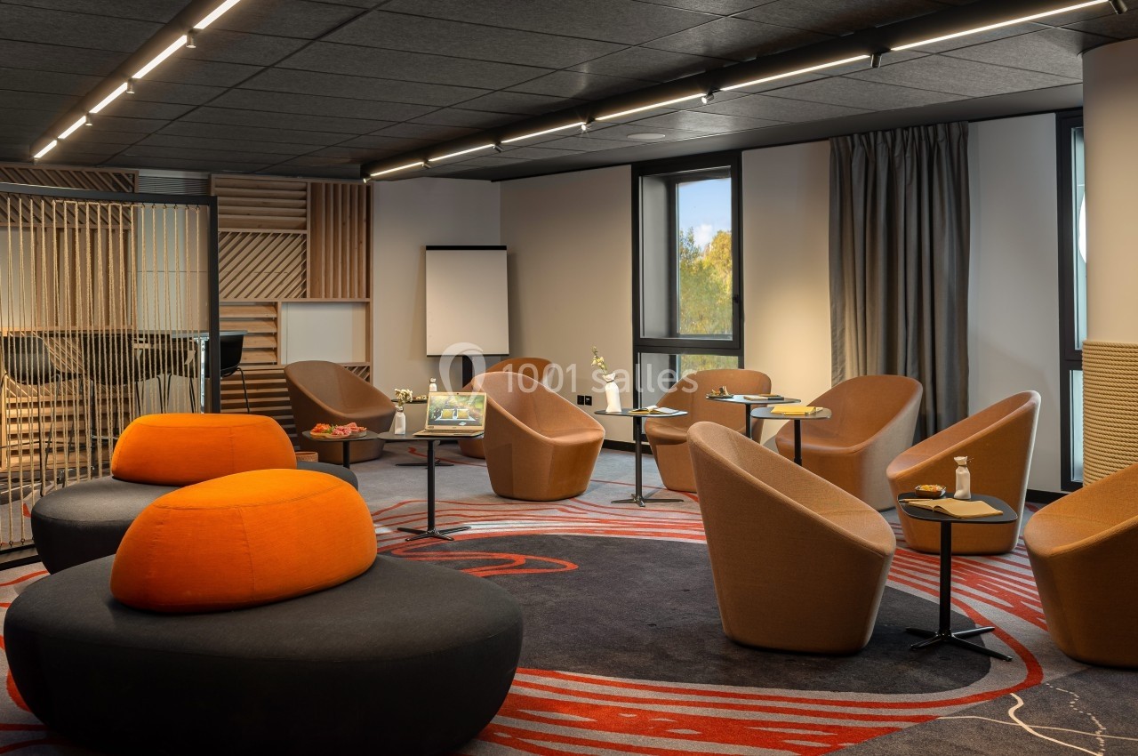 Salle de réunion moderne avec fauteuils, tables basses, tableau blanc et lumière naturelle.