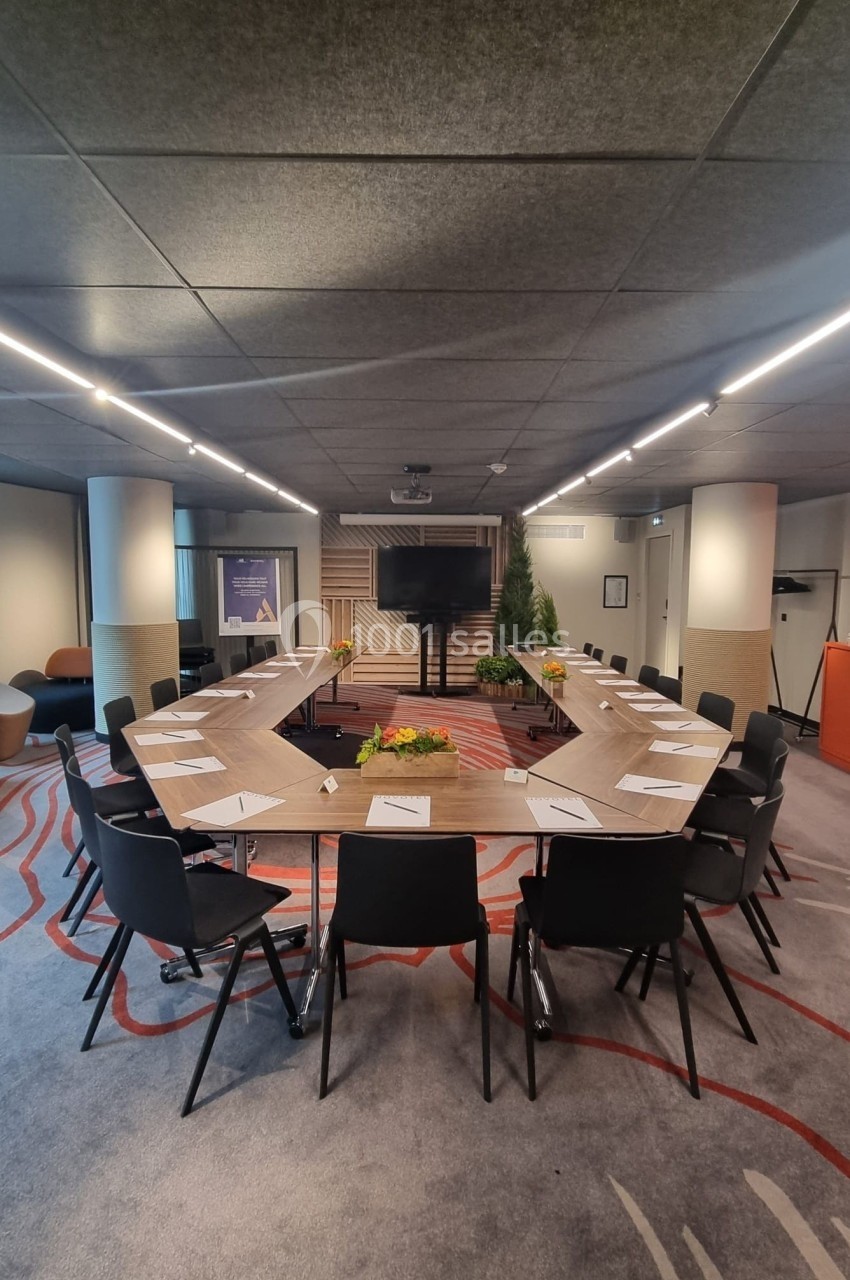 Salle de réunion moderne avec une grande table en U, des chaises noires et des documents disposés devant chaque place.
