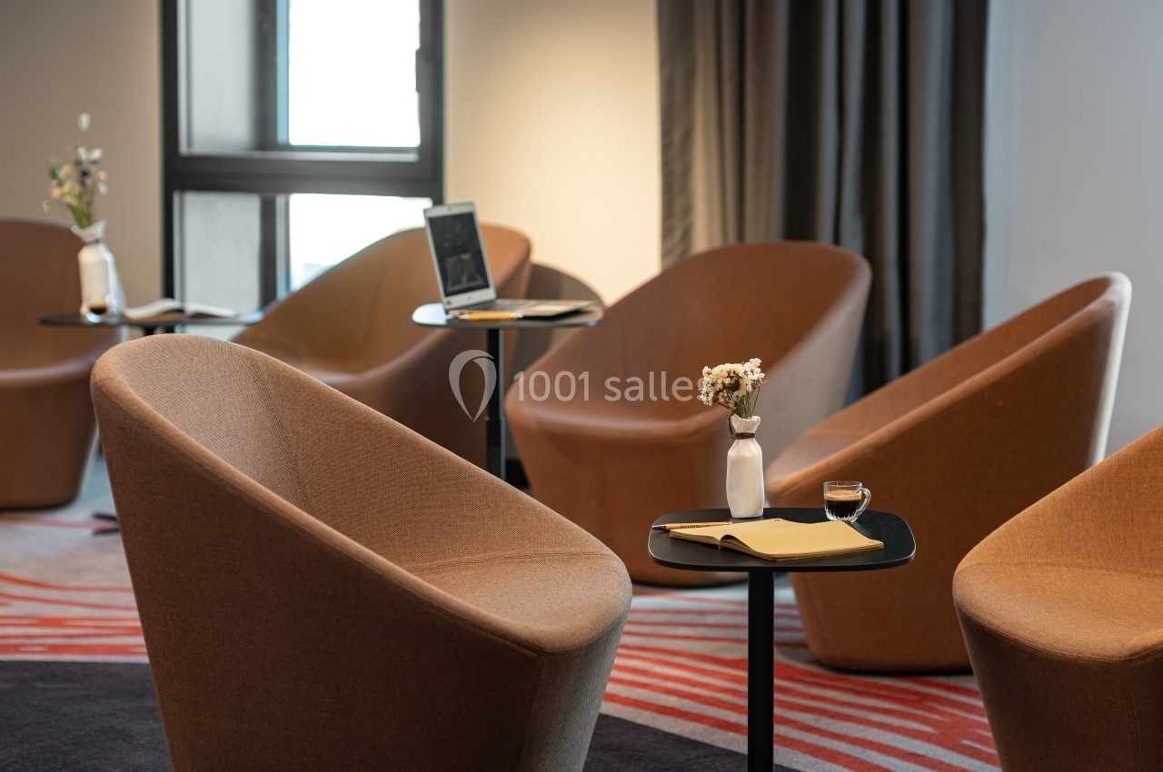 Salle avec fauteuils modernes, tables noires, carnets, fleurs en vase et lumière naturelle provenant d'une fenêtre.