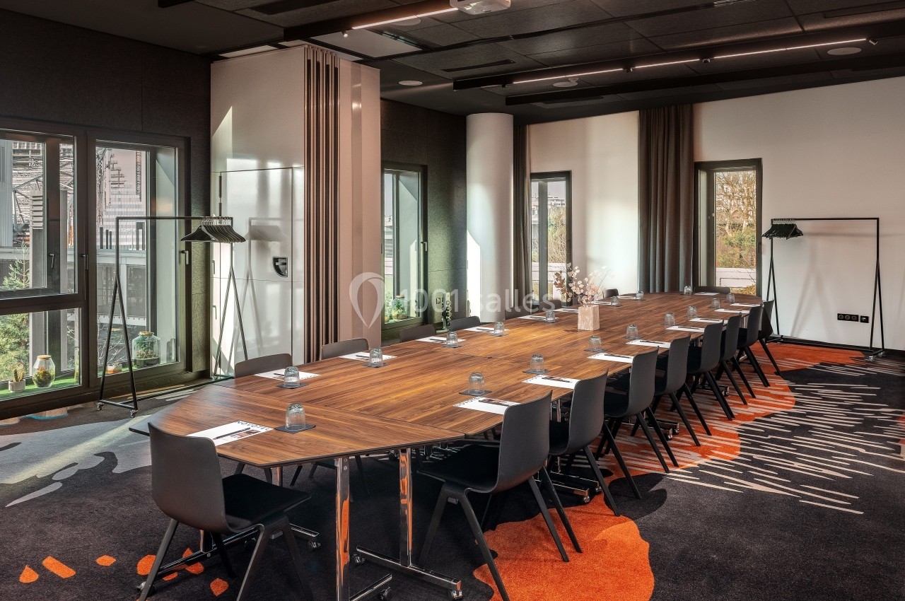 Salle de réunion moderne avec une grande table en bois, chaises noires, éclairage naturel et décoration contemporaine.