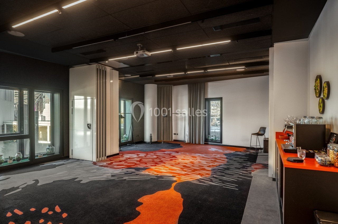 Salle de réunion moderne avec moquette colorée, cloisons amovibles, grandes fenêtres et éclairage suspendu.