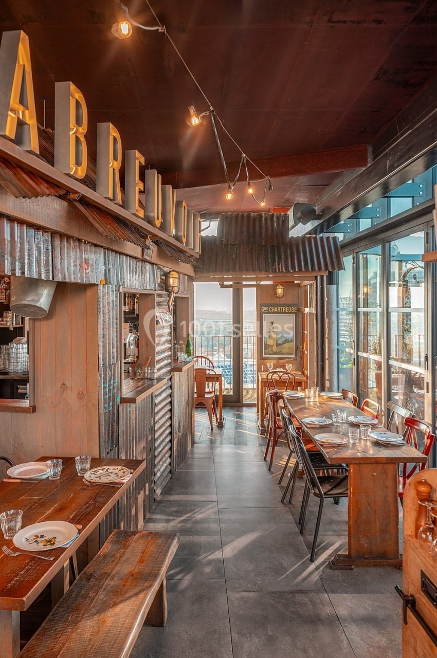 Salle de restaurant en bois avec tables dressées, grandes fenêtres et vue sur l'extérieur.