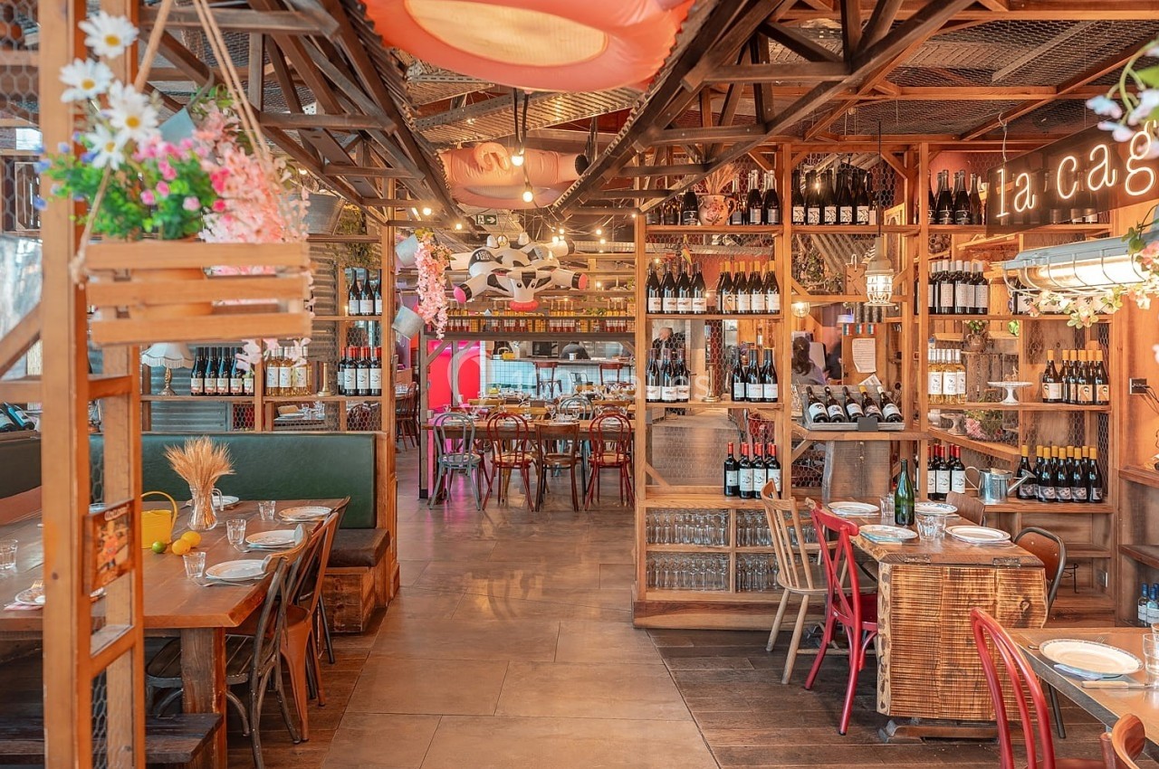 Intérieur d'un restaurant chaleureux avec tables en bois, étagères de bouteilles de vin et décoration florale.