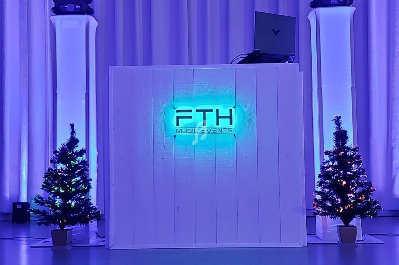 Pupitre de DJ lumineux entouré de deux sapins décorés, avec éclairages colorés sur des colonnes blanches.