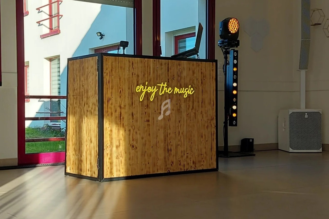 Console DJ en bois avec l'inscription lumineuse ’enjoy the music’, éclairée par la lumière naturelle d'une baie vitrée.