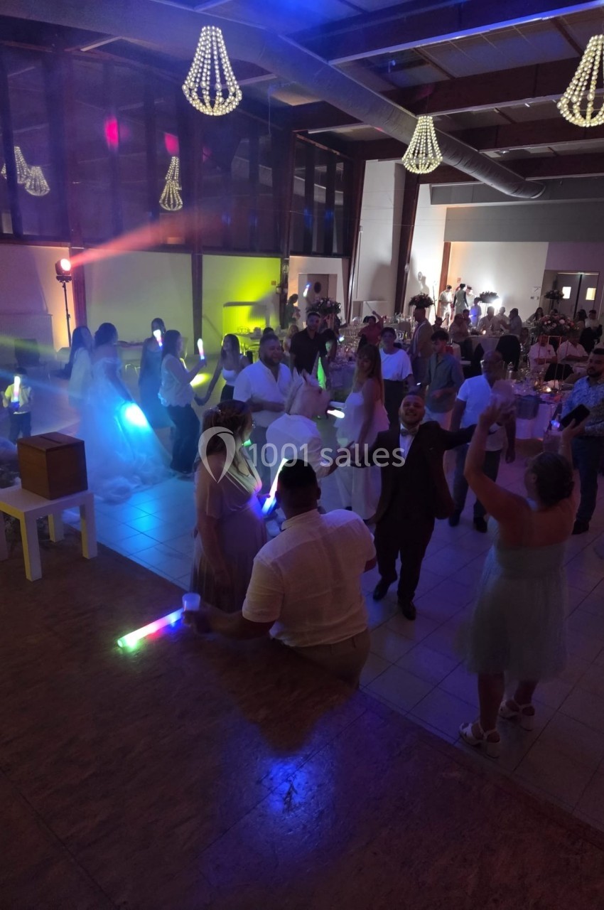 Personnes dansant dans une salle de réception éclairée par des lumières colorées et décorée de lustres suspendus.