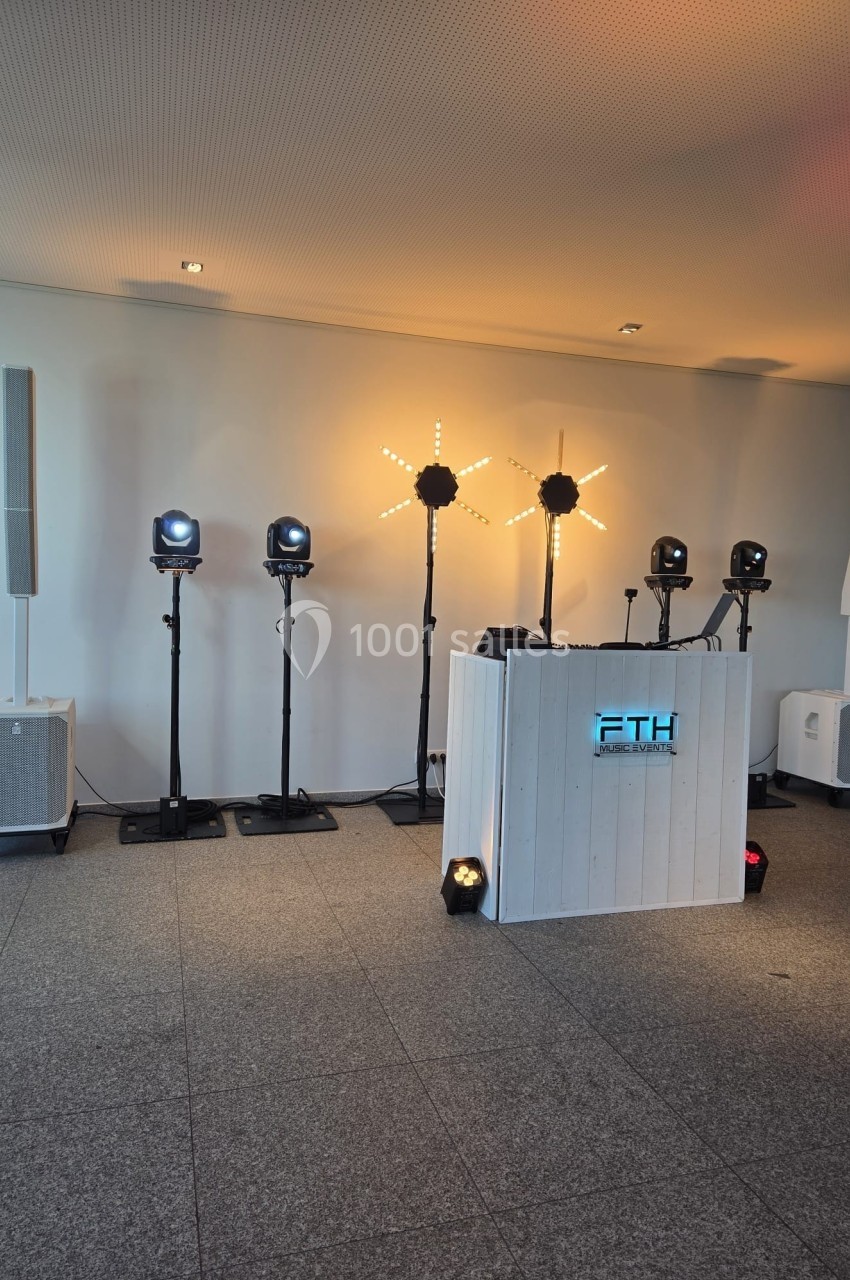 Installation de matériel de sonorisation et d'éclairage avec une cabine de DJ devant un mur blanc.