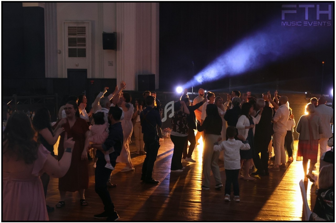 Des personnes dansent et socialisent dans une salle éclairée par des projecteurs, créant une ambiance festive.