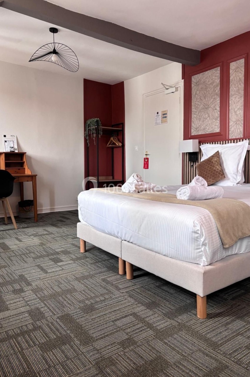 Chambre d'hôtel lumineuse avec lit double, bureau en bois, chaise noire et décoration murale rouge et beige.