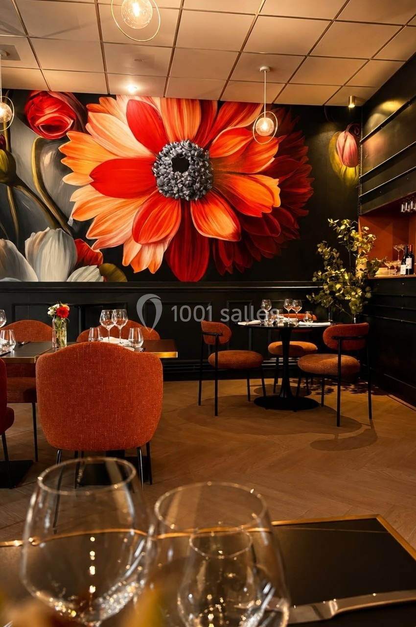 Salle de restaurant élégante avec mur décoré d'une fresque florale colorée et tables dressées avec verres et couverts.