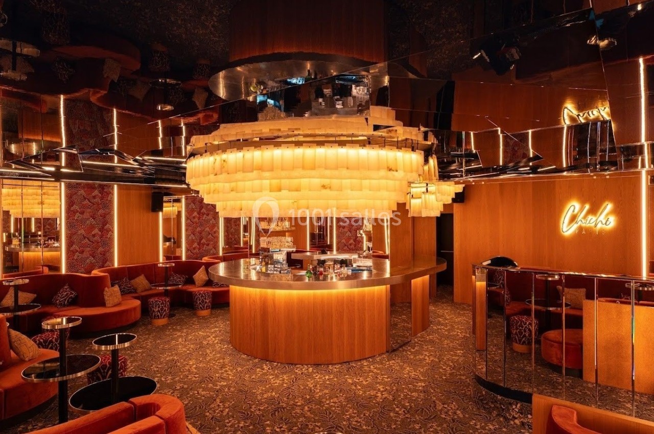 Bar circulaire éclairé par un grand lustre, entouré de sièges en velours et de miroirs dans une ambiance chaleureuse.