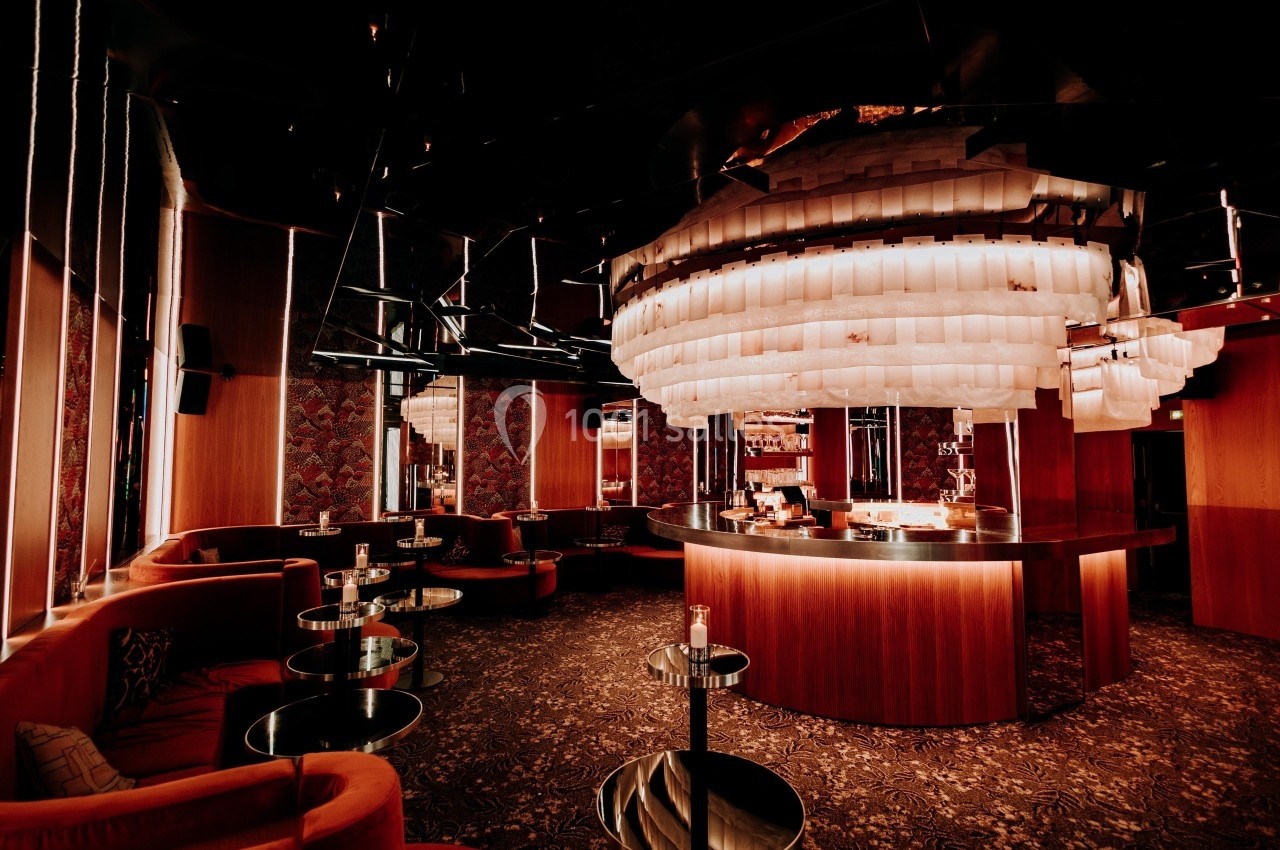 Bar élégant avec comptoir circulaire, éclairage tamisé et grand lustre moderne dans une ambiance chaleureuse.