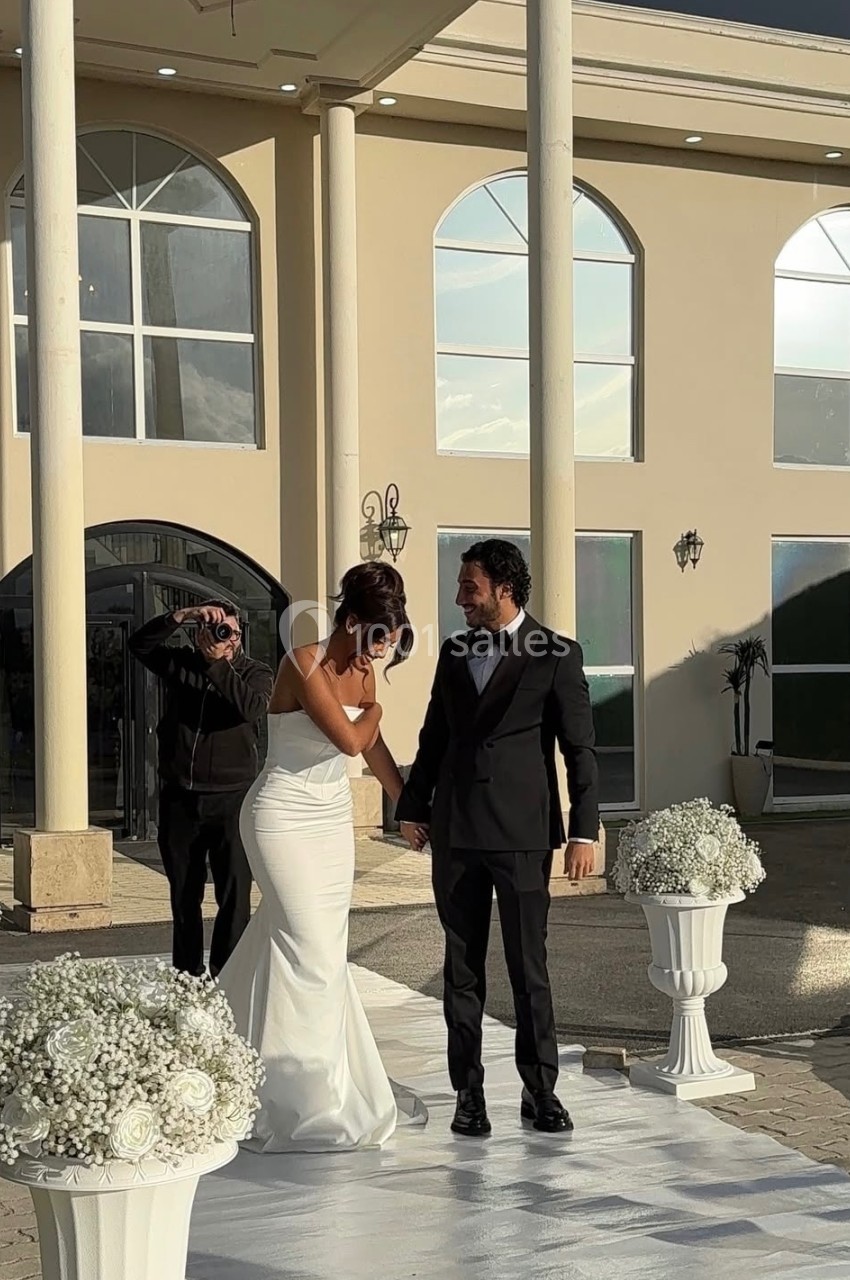 Un couple en tenue de mariage marche sur une allée blanche, entouré de décorations florales blanches.