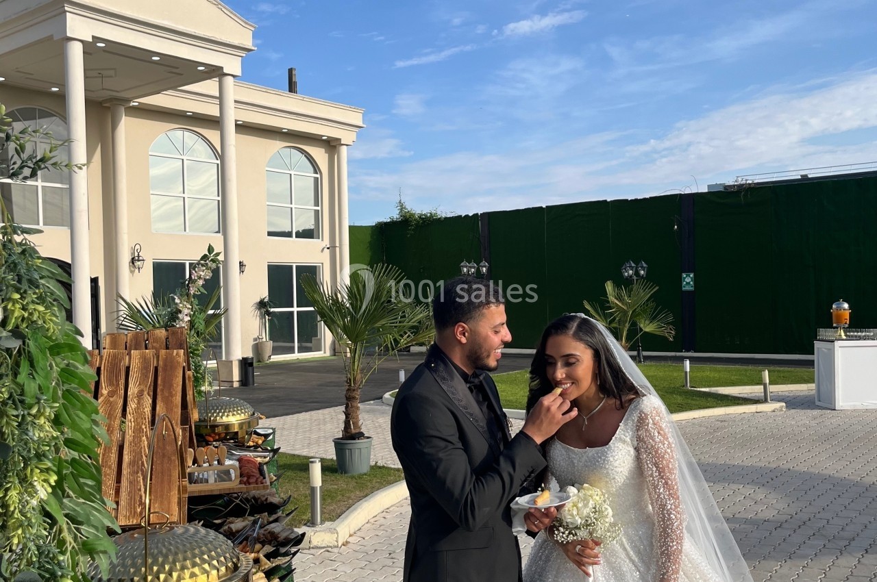 Un couple en tenue de mariage se tient devant un bâtiment élégant sous un ciel dégagé.