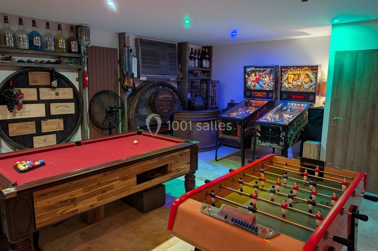 Salle de jeux avec billard, baby-foot, flippers et décorations de barriques et bouteilles de vin.
