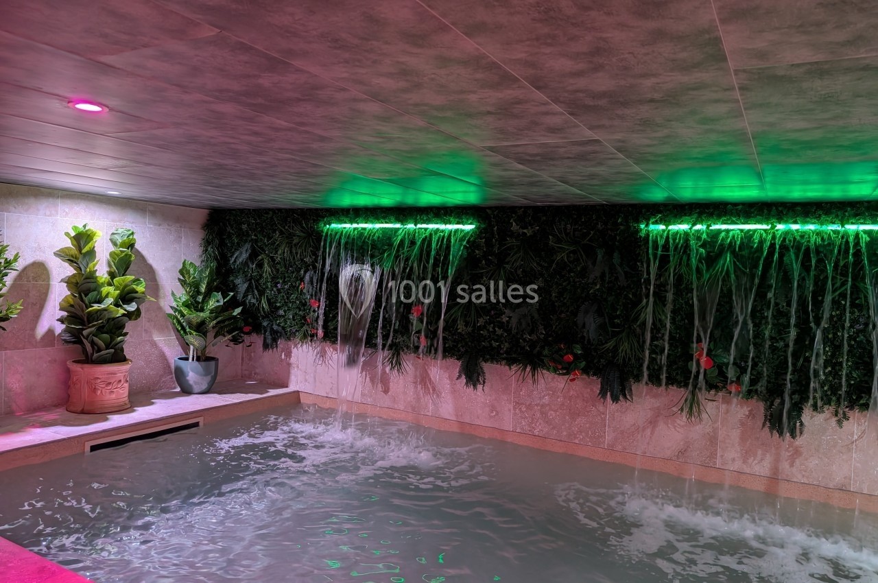 Mur végétal avec cascades lumineuses vertes au-dessus d'un bassin intérieur entouré de plantes décoratives.