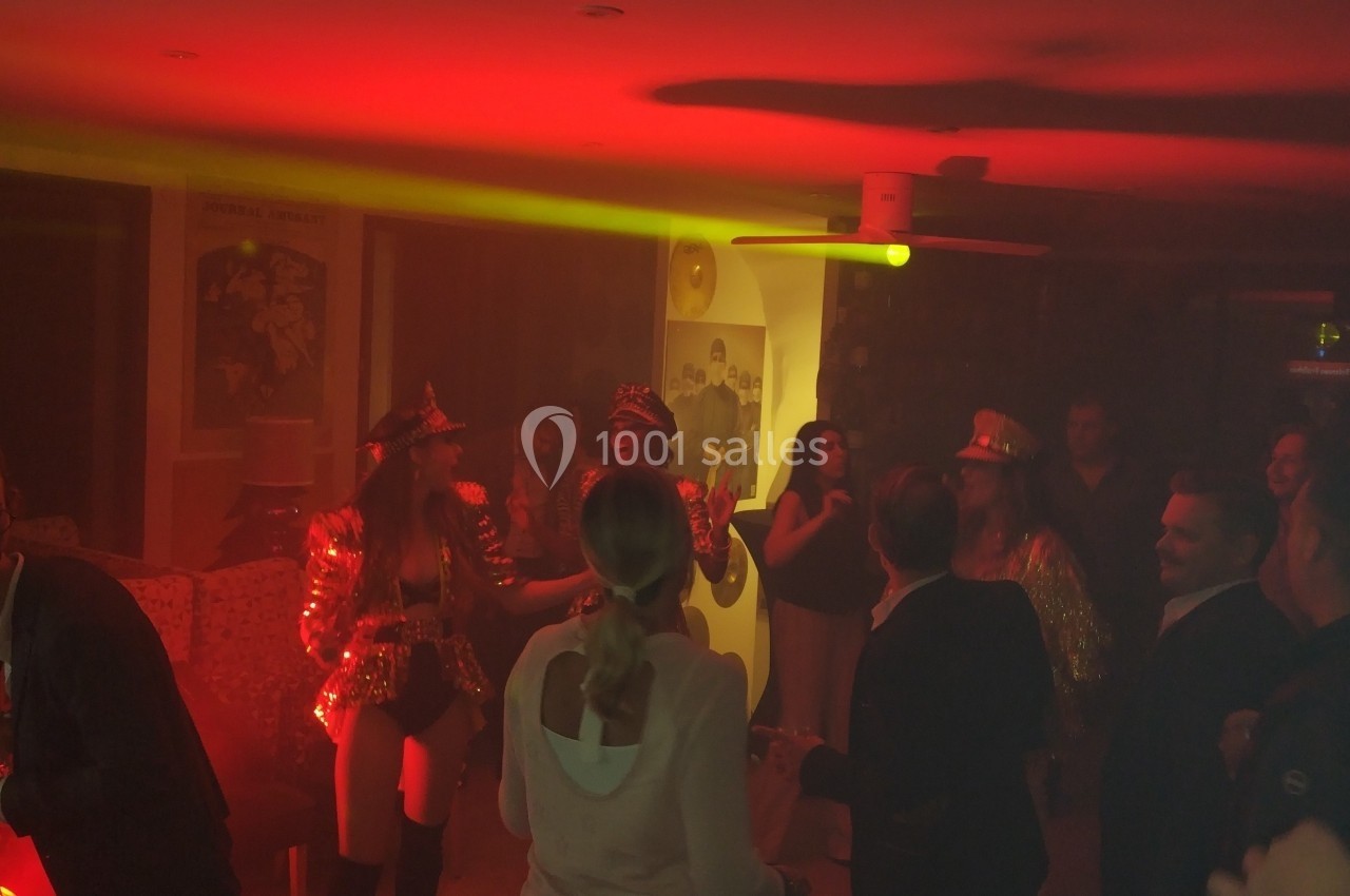 Groupe de personnes dans une pièce faiblement éclairée avec une lumière rouge, certaines déguisées, en train de danser et…