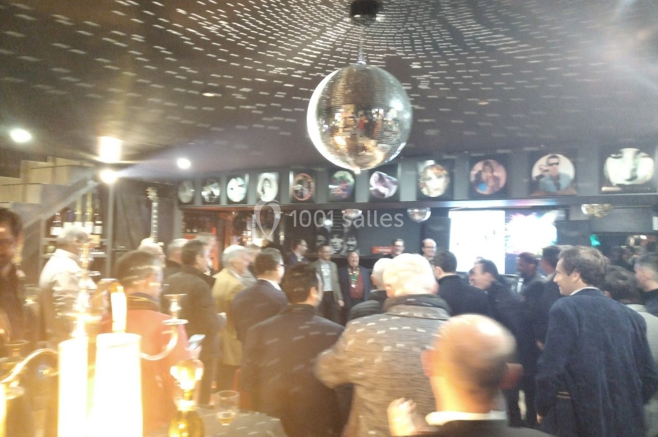 Groupe de personnes rassemblées dans un bar ou une salle avec une boule disco suspendue au plafond.