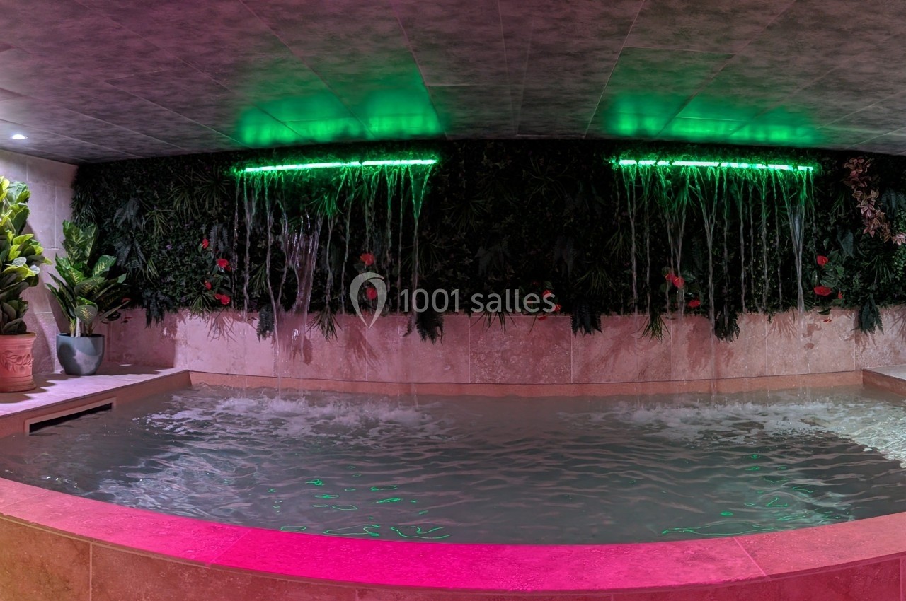 Piscine intérieure avec mur végétal illuminé par des néons verts et éclairage d'ambiance rose.