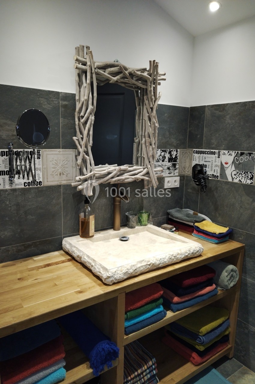 Meuble de salle de bain en bois avec vasque en pierre, miroir encadré de bois flotté et étagères garnies de serviettes…