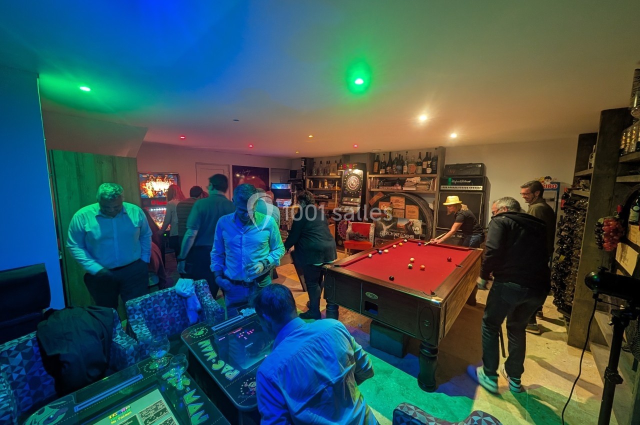Personnes jouant au billard et à des jeux d'arcade dans une salle de loisirs éclairée par des lumières colorées.