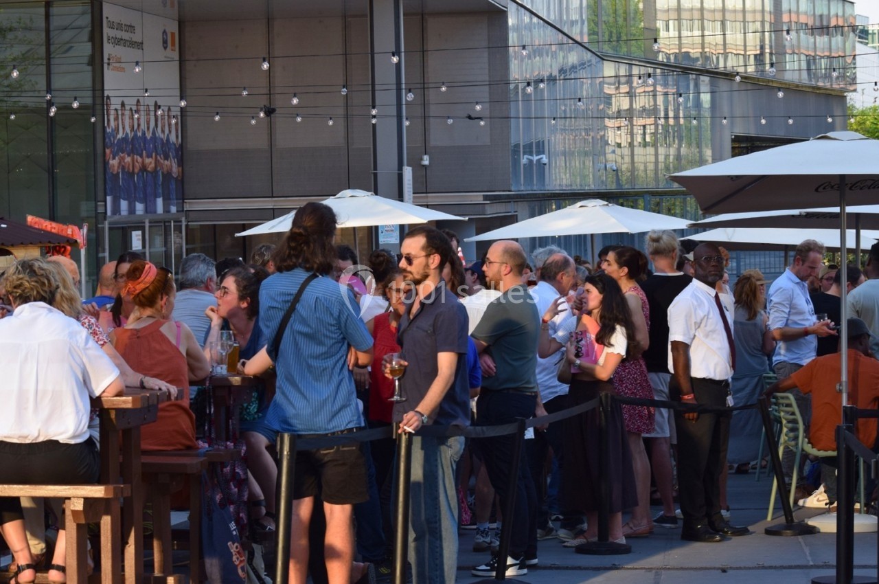 Groupe de personnes discutant et partageant des boissons en terrasse sous des parasols par une journée ensoleillée.