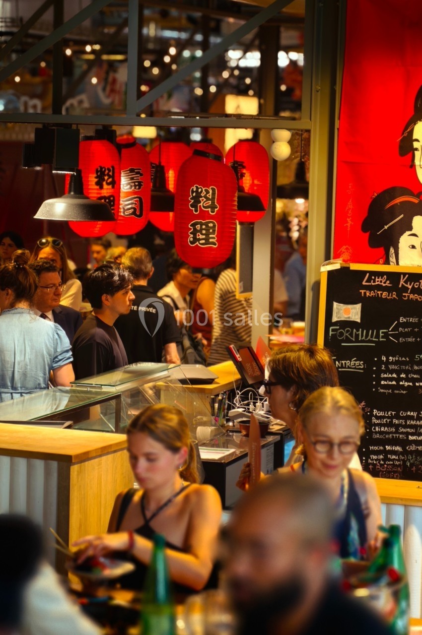 Des personnes dînent et discutent dans un restaurant animé décoré de lanternes rouges et d'affiches japonaises.