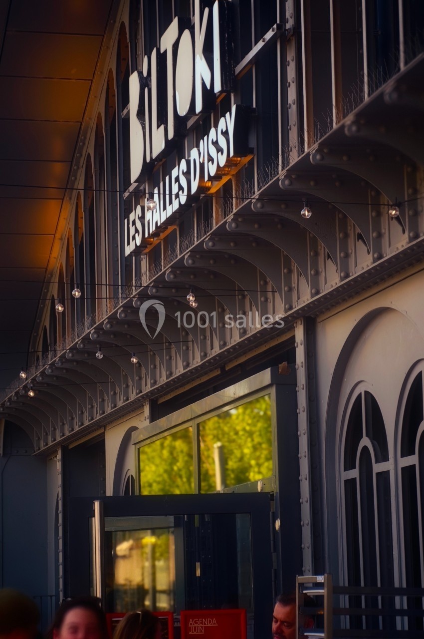 Façade des Halles d'Issy avec enseigne ’Biltoki’, architecture métallique et personnes en terrasse au premier plan.