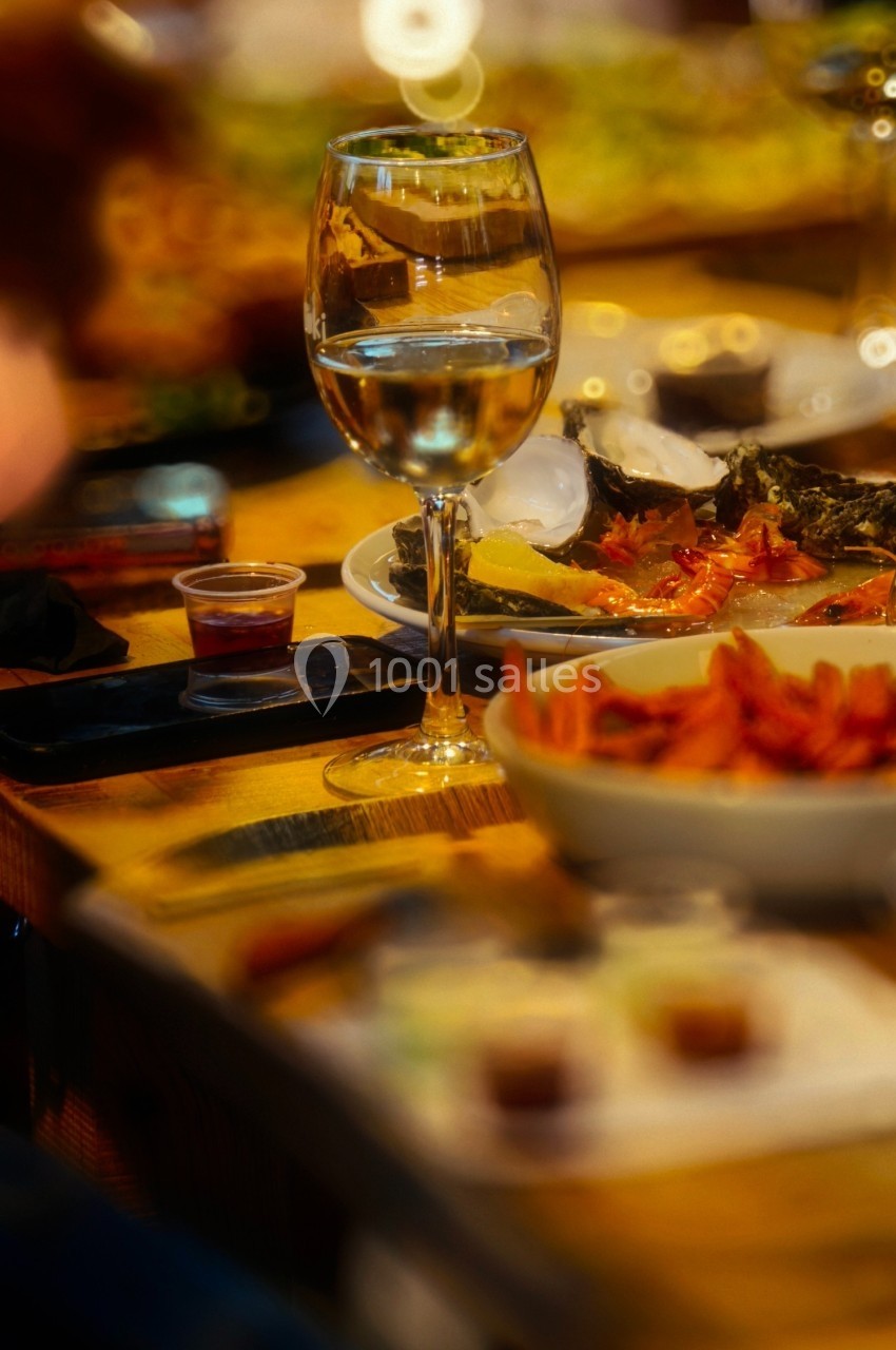 Verre d'eau sur une table en bois entourée de plats variés et d'autres verres lors d'un repas convivial.