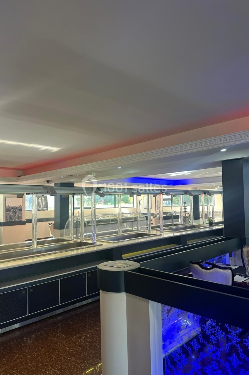 Salle de restaurant moderne avec un buffet vide, éclairage tamisé et décorations contemporaines.