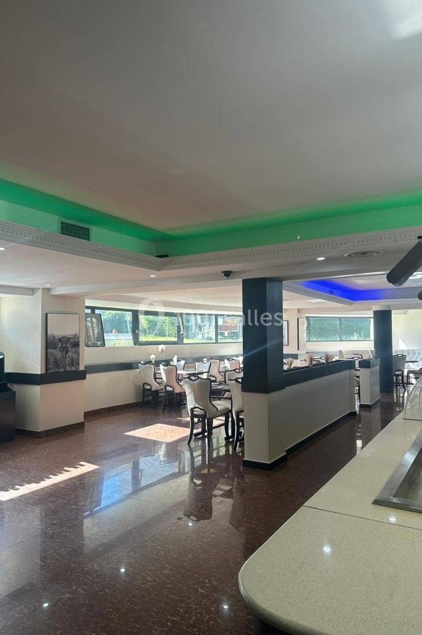 Salle de restaurant lumineuse avec tables et chaises disposées près de grandes fenêtres, éclairage au plafond.