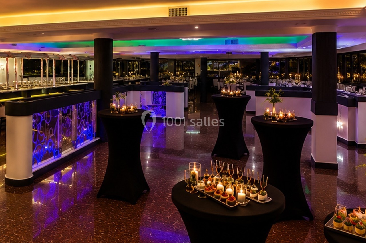 Salle de réception élégante avec tables hautes décorées de bougies et amuse-bouches, éclairage tamisé et coloré.