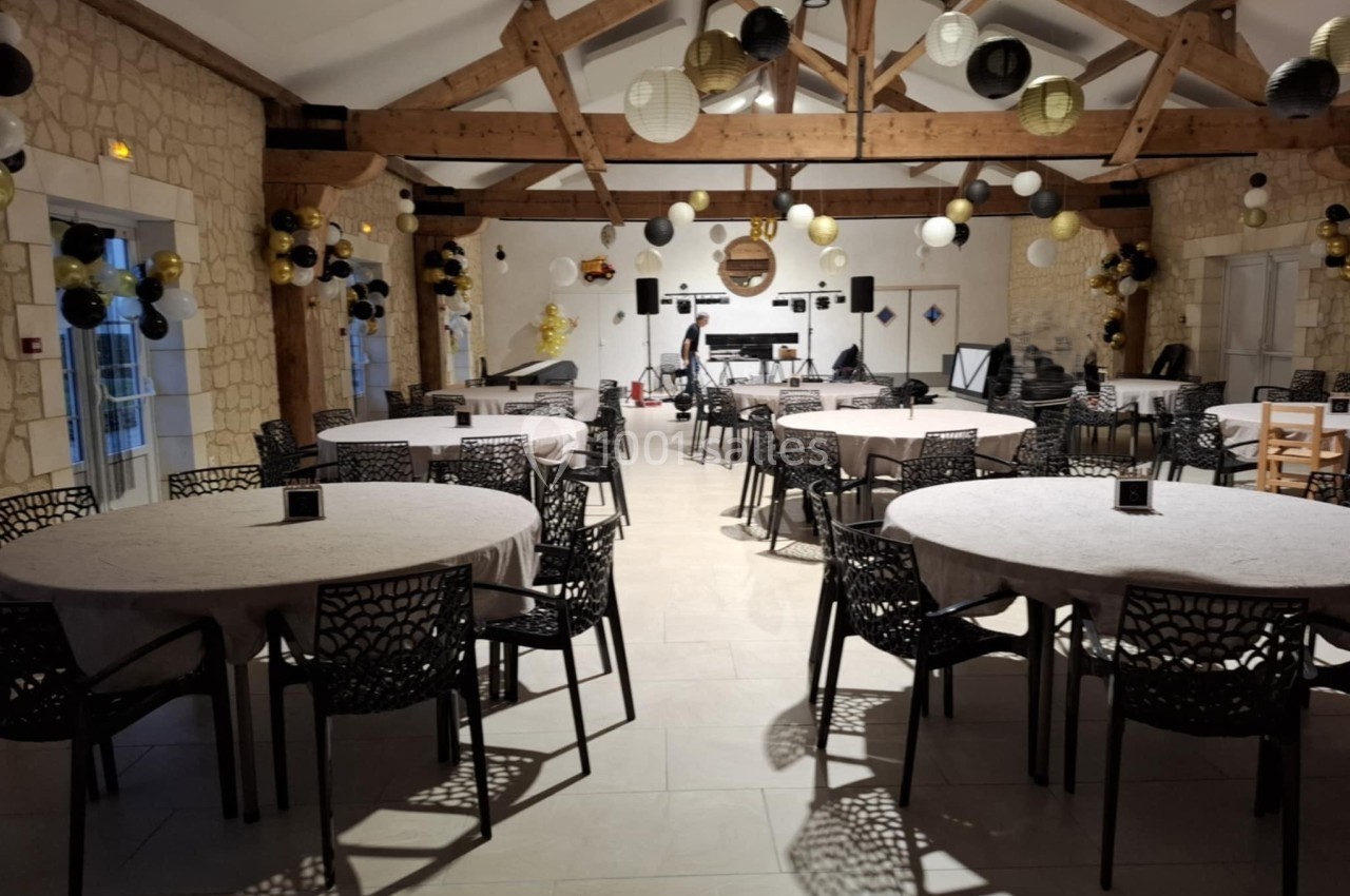 Salle de réception décorée avec des tables rondes, des chaises noires et des lanternes suspendues dans une ambiance festive.