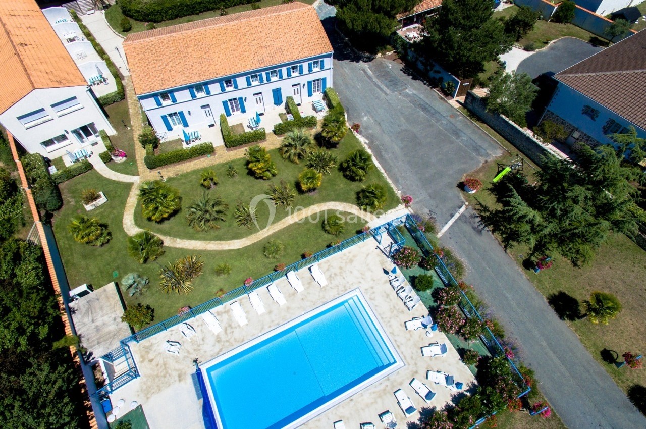 Vue aérienne d'une résidence avec jardin paysager, piscine extérieure et chaises longues disposées autour.
