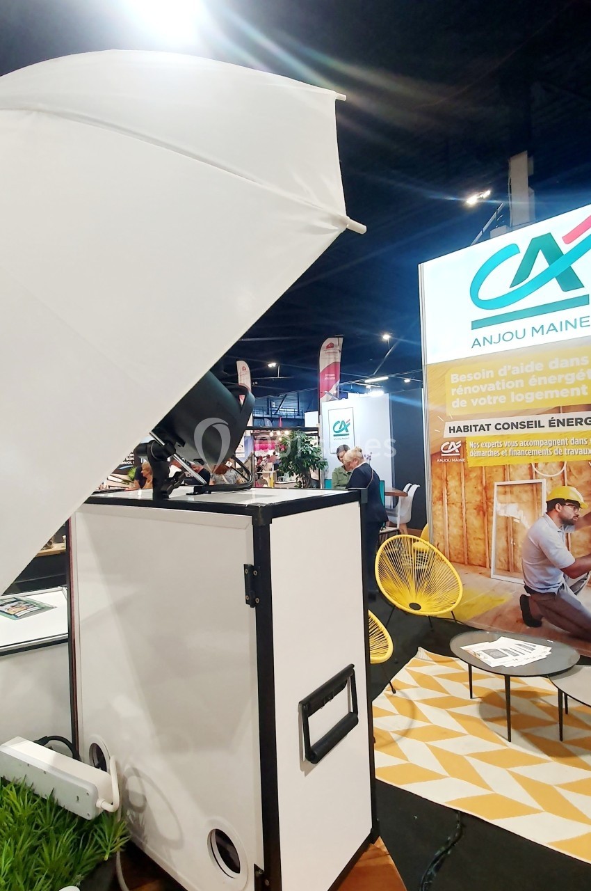 Stand d'exposition avec un panneau sur la rénovation énergétique, des fauteuils jaunes et un parapluie lumineux.