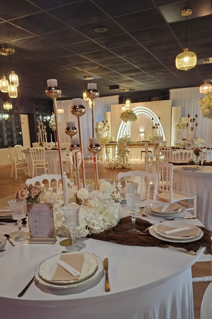 Salle de réception décorée avec des tables élégantes, des chandeliers dorés et un fond lumineux en arc.
