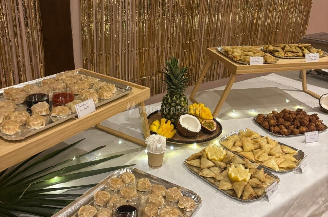 Buffet avec des plateaux de samoussas, bouchées vapeur, beignets et fruits exotiques sur une table décorée.