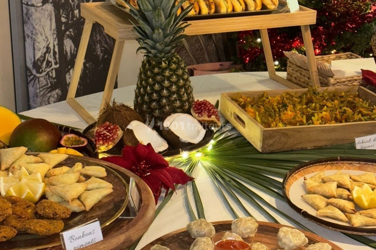 Buffet exotique avec fruits tropicaux, samoussas, bouchées et desserts variés sur une table décorée.