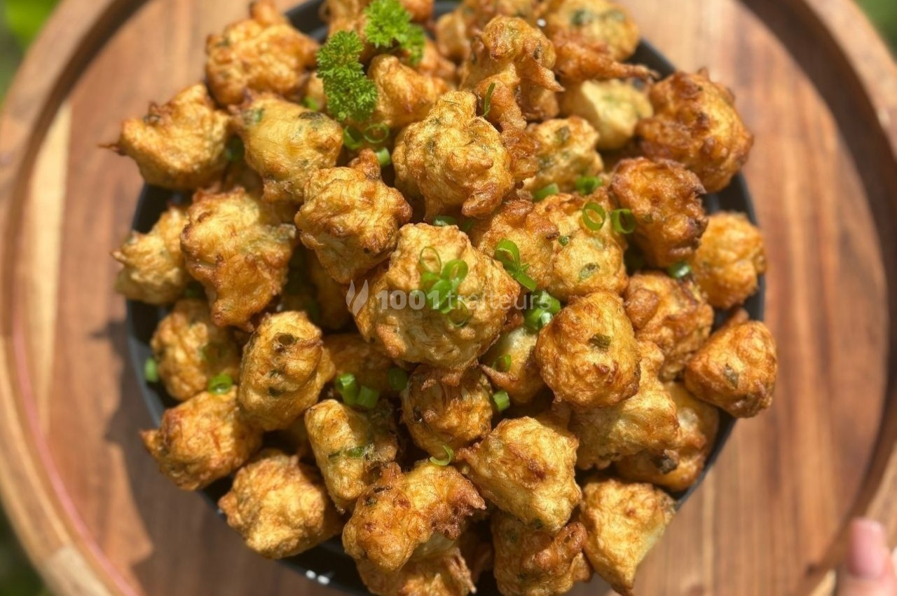Bol rempli de beignets dorés garnis de persil et de ciboulette, posé sur un plateau en bois.